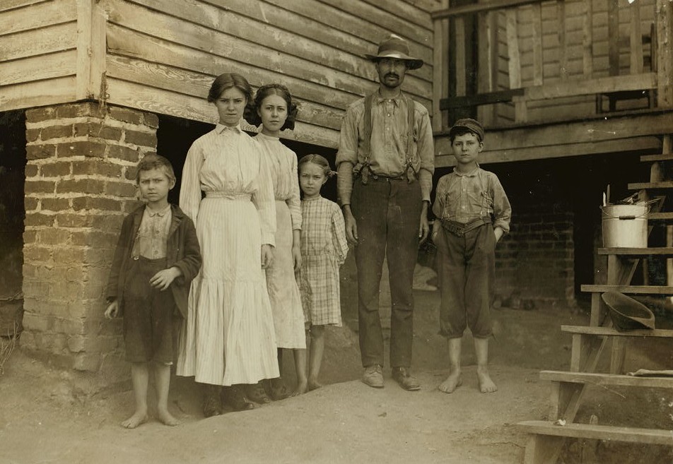 T.J. Fields and family. The father cards, two girls spin, boy on right end picks up bobbins, Washington Cotton Mills, Fries, Va. Been working a year or two. Mother and smallest children not in photo
